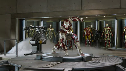HD PC desktop wallpaper from the Iron Man 3 movie: Iron Man in red-and-gold armor kneels on a lit platform in his workshop, with multiple suits displayed behind.