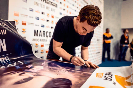 HD PC desktop wallpaper featuring music producer Hardwell signing a poster at an event, capturing his focused expression and the dynamic atmosphere.