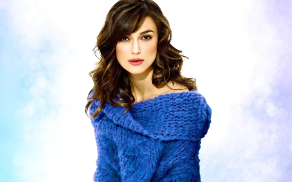 Keira Knightley poses elegantly in a blue sweater, featuring soft waves in her hair against a light backdrop. This image serves as an HD wallpaper for desktop backgrounds.