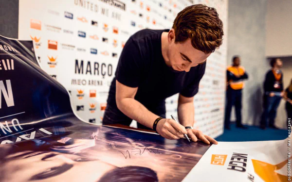 HD PC desktop wallpaper featuring music producer Hardwell signing a poster at an event, capturing his focused expression and the dynamic atmosphere.