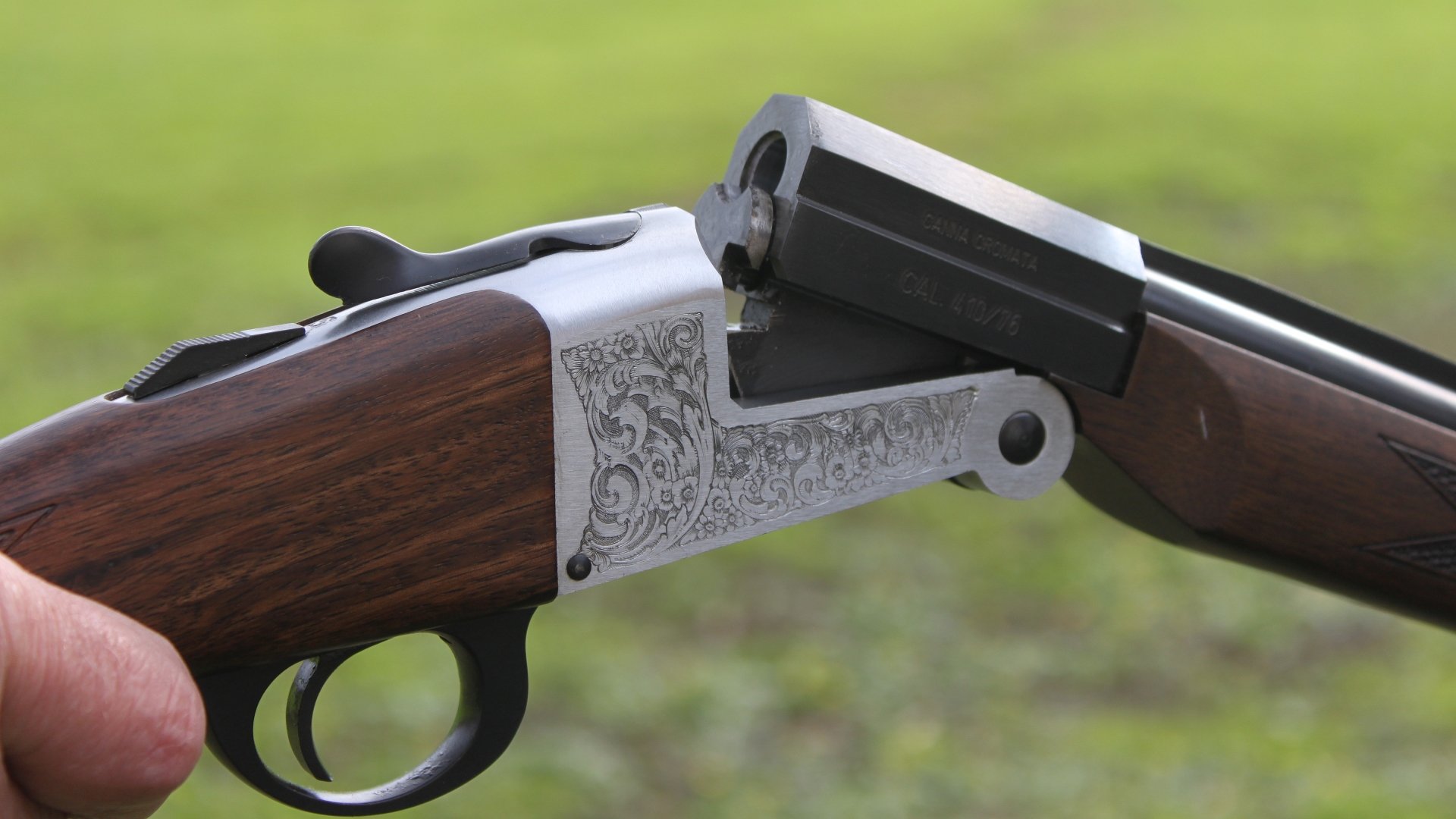 Close-up of a man-made shotgun with engraved metalwork, shown open against a blurred green background, rendered in 4K Ultra HD for PC desktop wallpaper.
