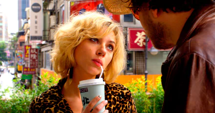 Scarlett Johansson as Lucy in a vibrant 4K Ultra HD movie wallpaper, sipping a drink in a bustling urban setting.