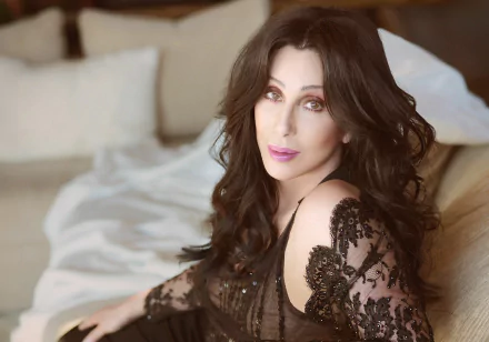 HD desktop wallpaper of American actress and singer Cher with long dark hair, wearing lipstick and a black lace top, posed elegantly in a softly lit room.