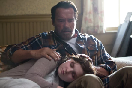 HD PC desktop wallpaper from the movie Maggie (2015): a weary, protective man sits on a couch with a young woman asleep across his lap, soft daylight filtering through a curtained window.