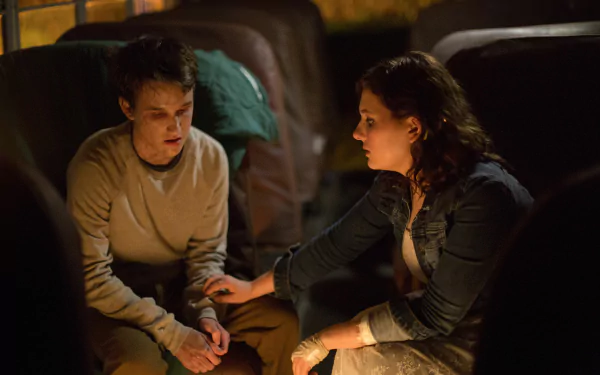 2K Quad HD PC desktop wallpaper from the movie Maggie (2015): two characters in a dim bus interior, one comforting the other by gently holding their hand.