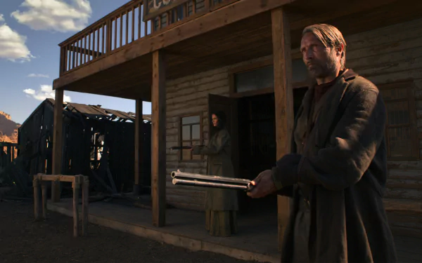 HD desktop wallpaper from the film The Salvation: a rugged man holds a double-barrel shotgun on a dusty western street while a woman watches from a saloon doorway.