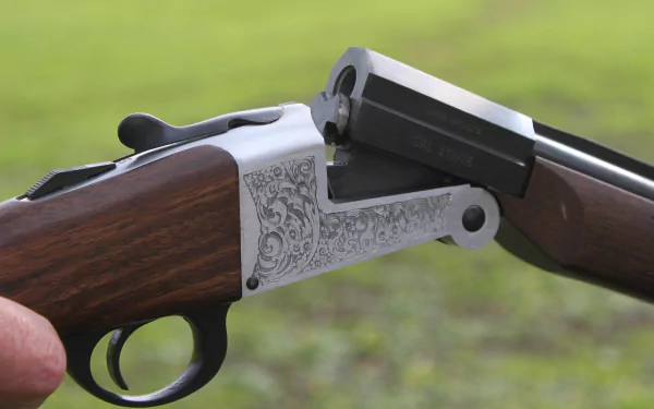 Close-up of a man-made shotgun with engraved metalwork, shown open against a blurred green background, rendered in 4K Ultra HD for PC desktop wallpaper.