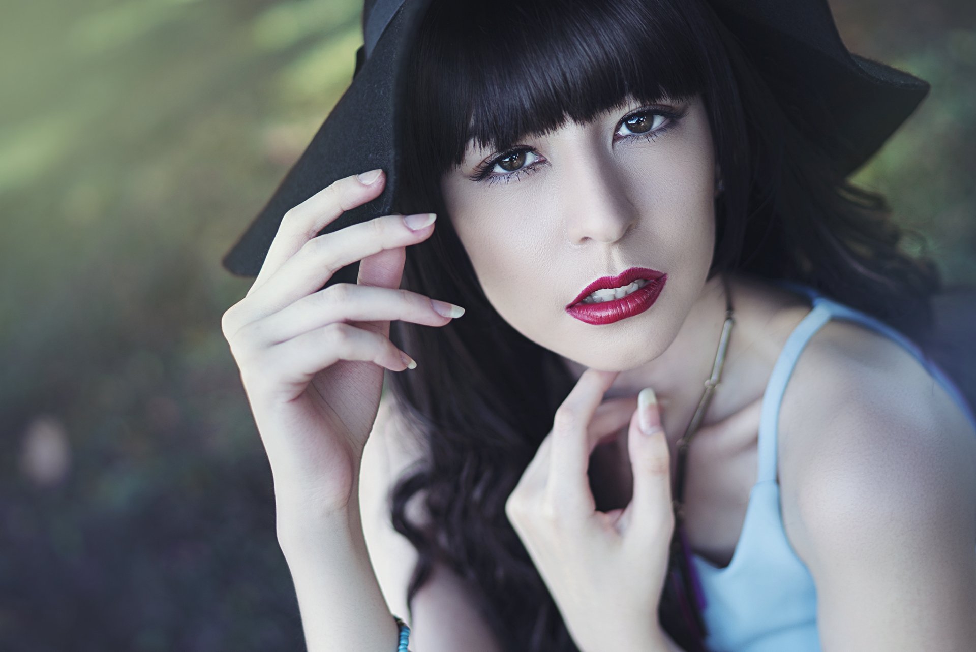 HD PC desktop wallpaper: a model woman with black hair, brown eyes and red lipstick wearing a hat, gazing up as her hands gently frame her face.