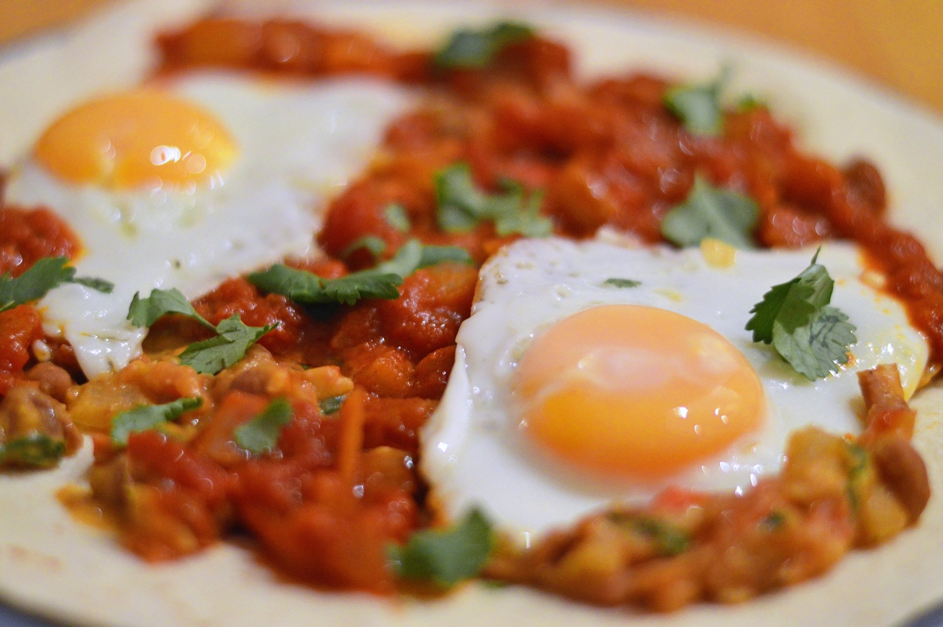 5K Ultra HD PC desktop wallpaper: close-up food shot of two sunny-side-up eggs on a rich tomato and pepper stew, garnished with fresh herbs.