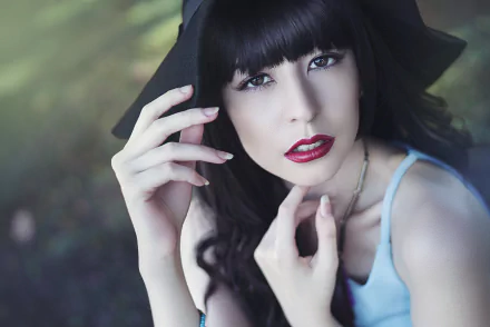 HD PC desktop wallpaper: a model woman with black hair, brown eyes and red lipstick wearing a hat, gazing up as her hands gently frame her face.