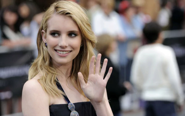 Emma Roberts waves and smiles at an event, showcasing her stylish look. This vibrant image serves as a 4K Ultra HD desktop wallpaper and background for fans.
