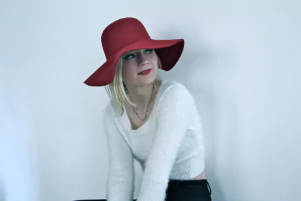 Celebrity Emily Kinney poses wearing a red wide-brim hat and white sweater in this 4K Ultra HD PC desktop wallpaper and background.