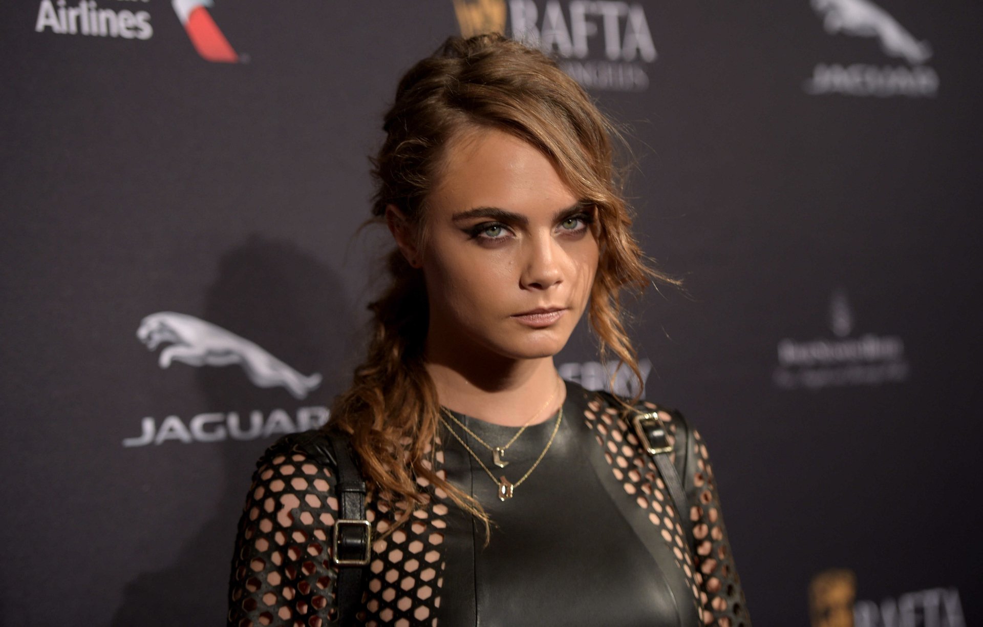 A striking 4K Ultra HD image of Cara Delevingne, an English model and actress with blue eyes and blonde hair, posing confidently at a red carpet event.