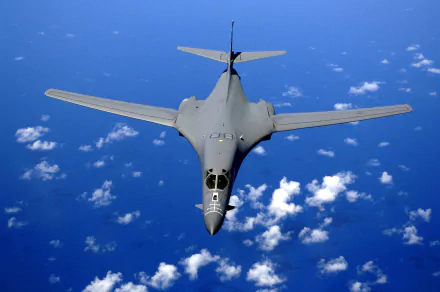 HD desktop wallpaper of a Rockwell B-1 Lancer military bomber flying above scattered clouds over the ocean.