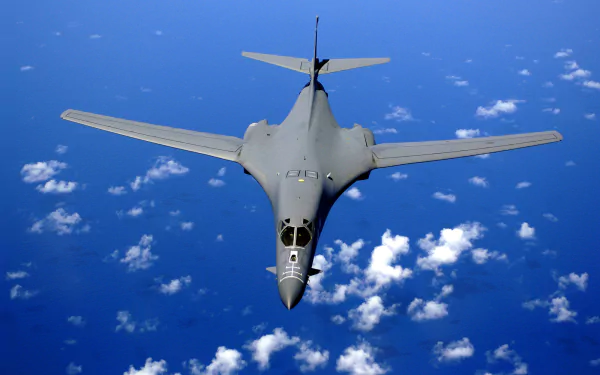 HD desktop wallpaper of a Rockwell B-1 Lancer military bomber flying above scattered clouds over the ocean.