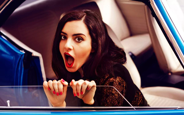 HD PC desktop wallpaper featuring Charli XCX with an expressive pose inside a blue car, capturing a vibrant and dynamic music-themed aesthetic.