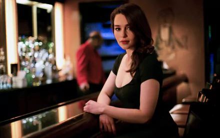 Emilia Clarke poses elegantly at a bar, exuding charm and sophistication in this HD desktop wallpaper. The soft lighting creates a captivating ambiance.