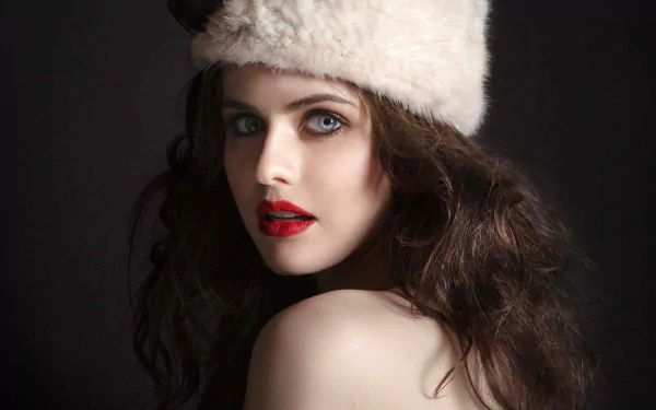 HD desktop wallpaper featuring actress Alexandra Daddario with wavy dark hair, wearing a fur hat and red lipstick, posing against a dark background.
