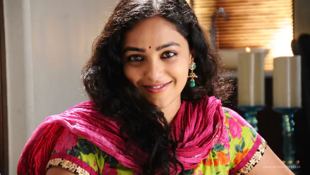 HD desktop wallpaper featuring celebrity Nithya Menon smiling warmly, dressed in a colorful traditional outfit with a pink dupatta.