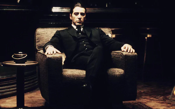HD PC desktop wallpaper featuring a scene from the movie The Godfather: Part II, showing a man in a dark suit seated confidently in an armchair.