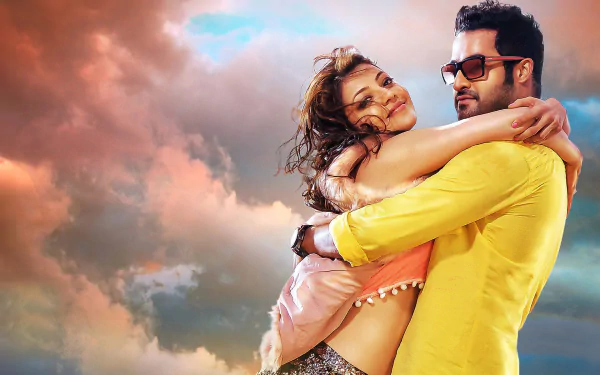 Kajal Aggarwal and N. T. Rama Rao Jr. share a warm embrace in this HD wallpaper from the movie Temper, set against a vibrant sky.