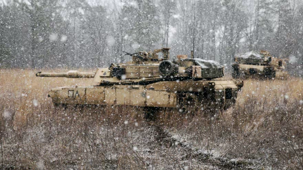 An M1 Abrams tank positioned in a snowy field, surrounded by falling snowflakes. This HD wallpaper captures the essence of military might in a serene winter landscape.