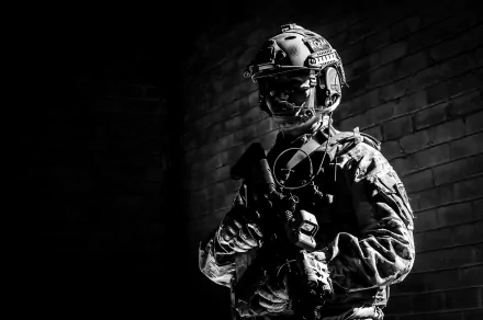 A monochrome image of a soldier in tactical gear, standing with a weapon, set against a dark brick background, making for a striking military-themed HD desktop wallpaper.