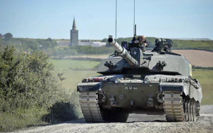 Military HD PC desktop wallpaper of a Challenger 2 main battle tank rolling down a rural road with crew on top, church spire and fields in the background.