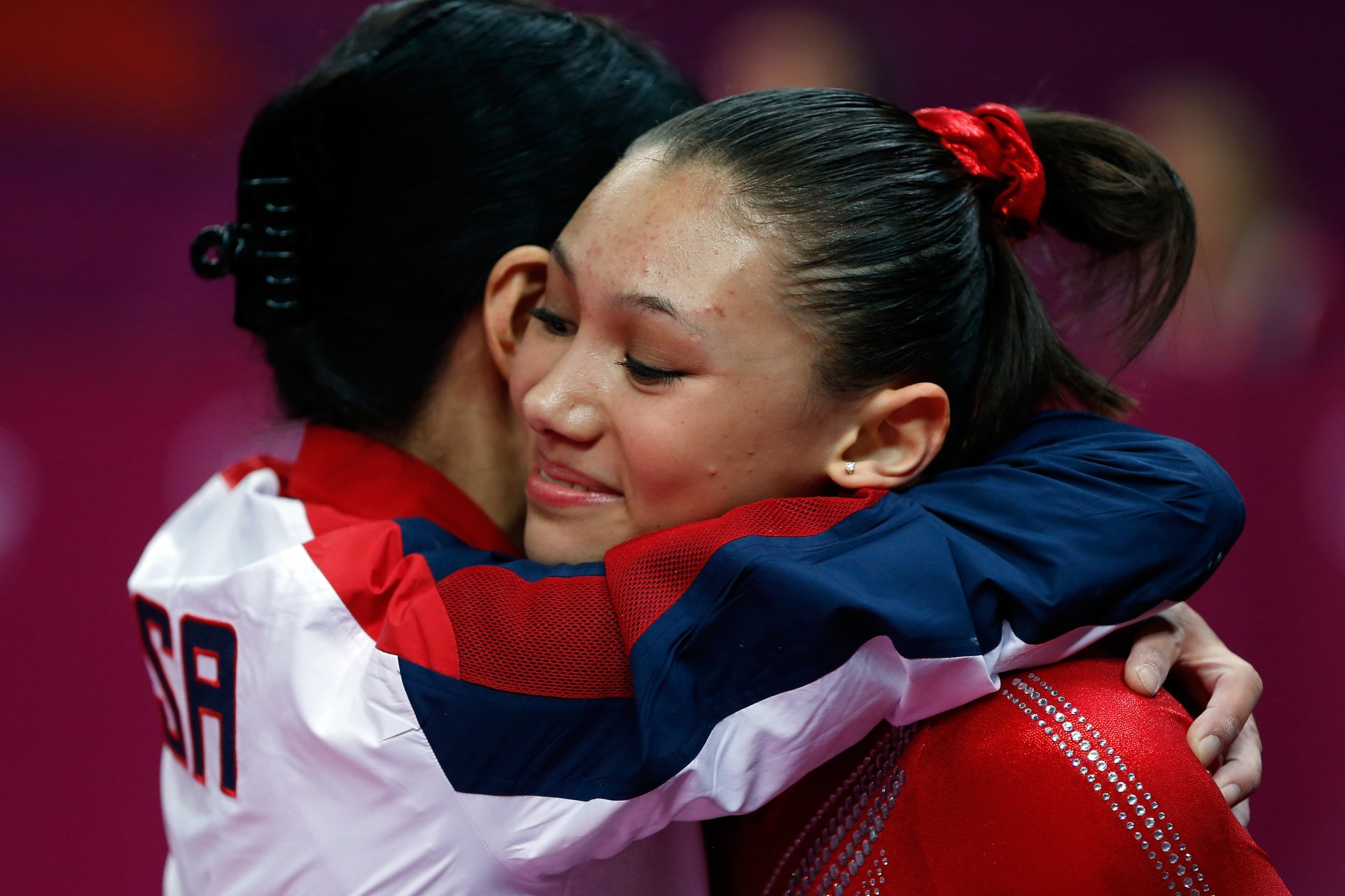 Olympic Games gymnasts hug after a performance, one wearing a Team USA jacket — vivid 5K Ultra HD sports desktop wallpaper.