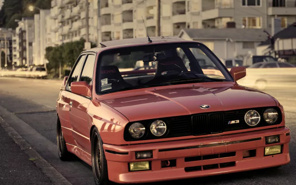 Red BMW M3 E30 on a sunlit city street — HD PC desktop wallpaper/background featuring a classic sports sedan.