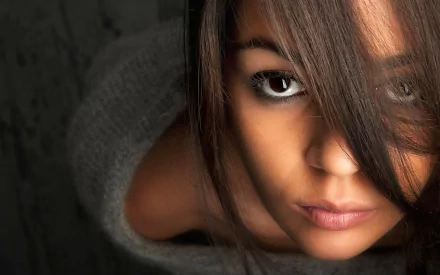 A high-definition desktop wallpaper featuring a close-up of a woman's face, with an intense gaze and partial coverage of her eye by her hair, creating a striking visual.