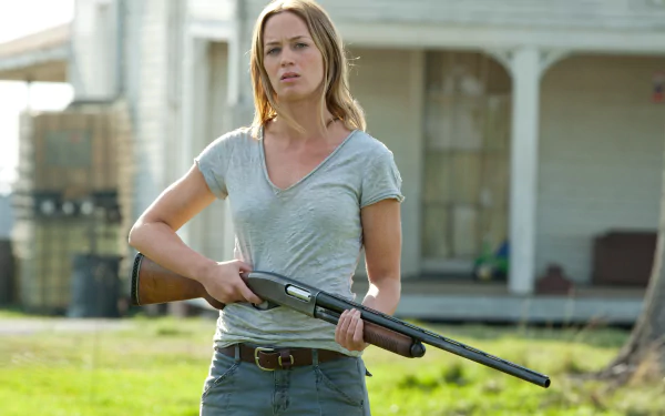 HD desktop wallpaper featuring Emily Blunt holding a shotgun in a scene from the movie Looper, set against a rural background.