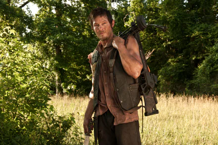 Norman Reedus as Daryl Dixon stands confidently in a grassy field, holding a crossbow, capturing the essence of his character from the TV show The Walking Dead in this HD wallpaper.
