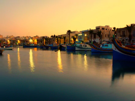 Man-made Marsaxlokk harbor at sunset, colorful luzzu boats reflecting on calm water — 2K Quad HD PC desktop wallpaper and background.