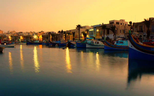 Man-made Marsaxlokk harbor at sunset, colorful luzzu boats reflecting on calm water — 2K Quad HD PC desktop wallpaper and background.