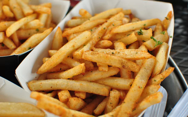 A close-up 4K Ultra HD PC desktop wallpaper of golden, seasoned French fries served in a paper tray, highlighting their crispy texture and vibrant color.
