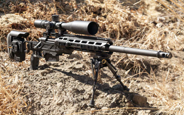 2K Quad HD PC desktop wallpaper/background of a man-made modern sniper rifle on a bipod resting on dry earth and grass.