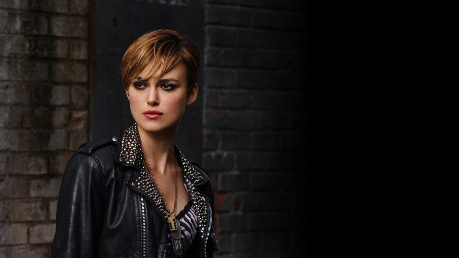 HD PC desktop wallpaper featuring actress Keira Knightley in a leather jacket against a dark, textured brick background.