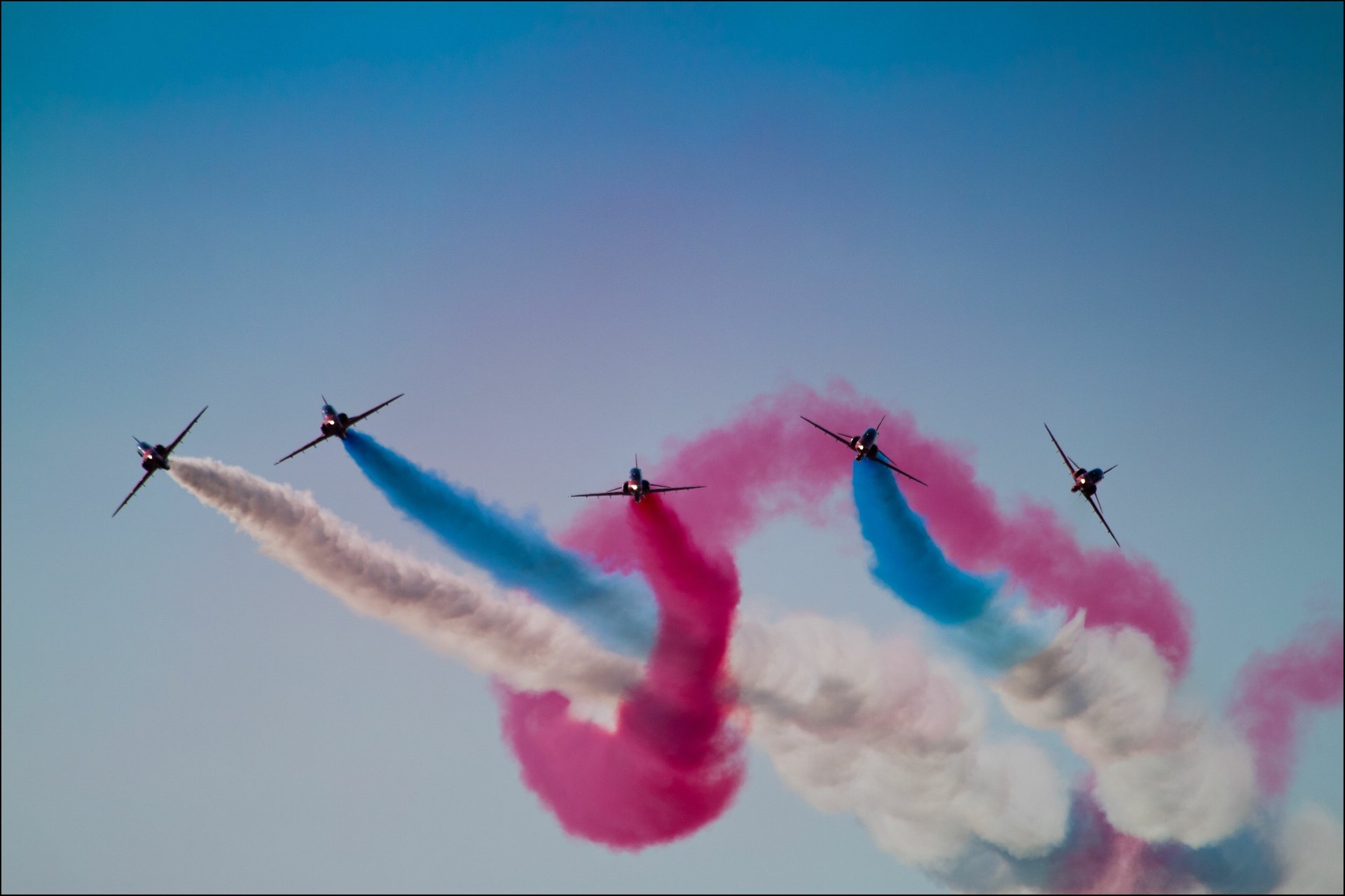 Military jets in an air show twist through the sky, leaving red, white and blue smoke trails — 5K Ultra HD PC desktop wallpaper/background.