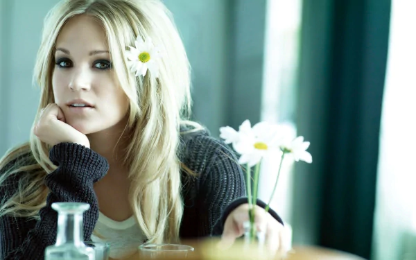 HD PC desktop wallpaper featuring music artist Carrie Underwood with blonde hair, wearing a dark sweater, holding a daisy, and a blurred background.