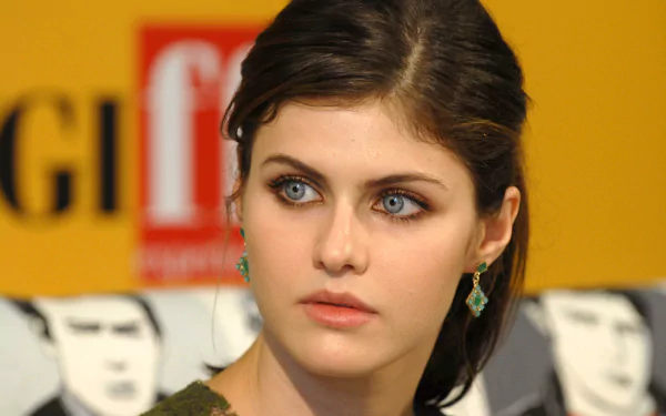 HD desktop wallpaper featuring actress Alexandra Daddario with black hair and blue eyes, in front of a yellow background.