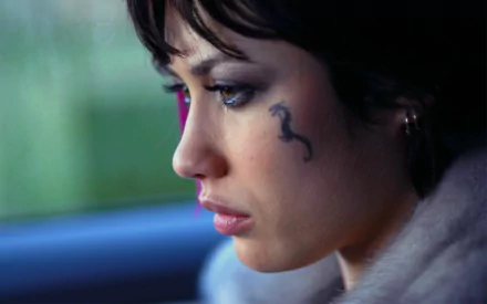 Close-up of actress Olga Kurylenko with a distinct facial tattoo, gazing thoughtfully. This high-definition image serves as a striking desktop wallpaper and background.