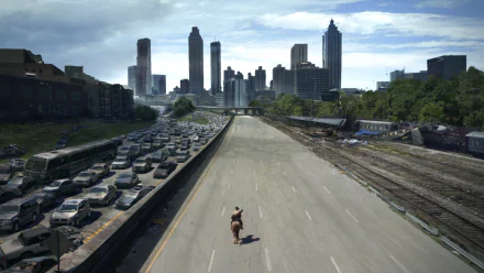 Rick Grimes rides through a deserted highway, city skyline in the distance, capturing the post-apocalyptic vibe of The Walking Dead in this HD desktop wallpaper.