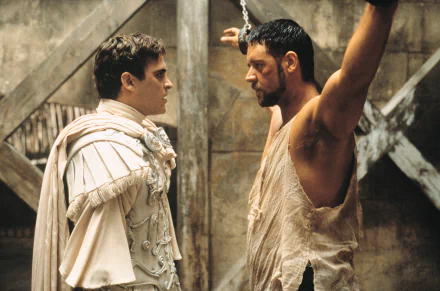 HD desktop wallpaper featuring Joaquin Phoenix and Russell Crowe in a scene from the movie Gladiator. Phoenix is dressed in white armor while Crowe stands restrained with arms raised.