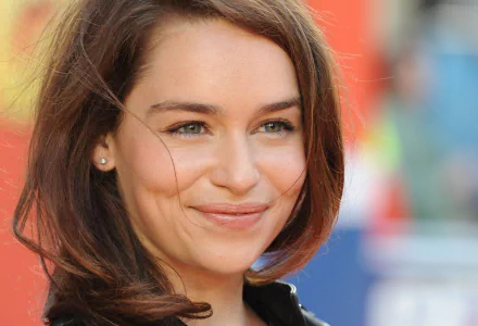 A close-up of Emilia Clarke smiling, showcasing her expressive eyes and wavy hair, set against a colorful background. This image serves as a vibrant HD desktop wallpaper.