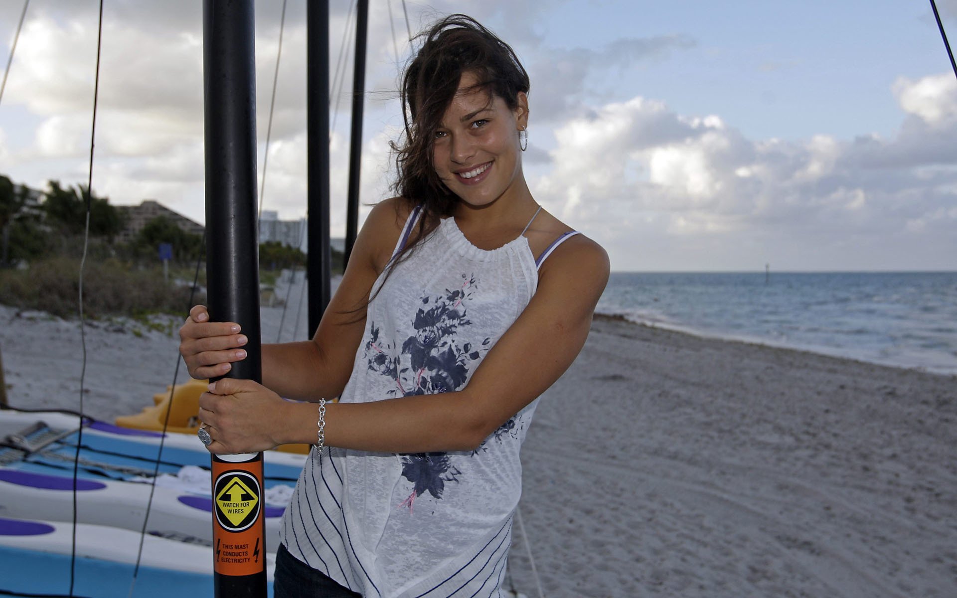 Ana Ivanovic smiles while posing with a boat mast on the beach, showcasing her sporty vibe against a serene seaside backdrop. A vibrant HD desktop wallpaper for sports enthusiasts.