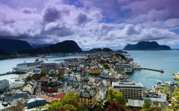 Aerial view of Ålesund, Norway, showcasing the town's man-made structures nestled between fjords and mountains under a dramatic cloudy sky.