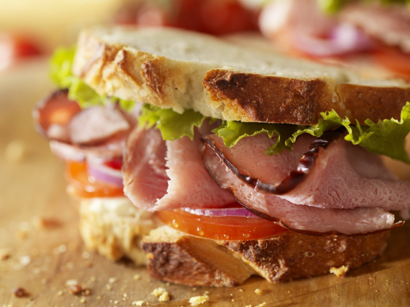 HD desktop wallpaper featuring a close-up of a fresh sandwich with layers of sliced meat, lettuce, tomato, and onion on rustic bread.