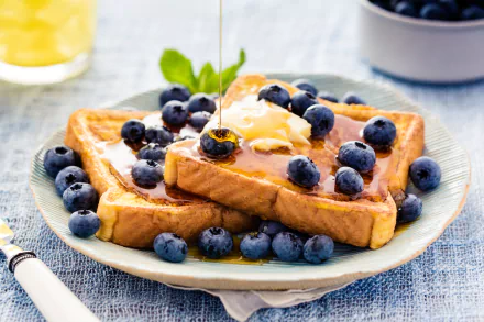 A delicious plate of golden French toast topped with fresh blueberries, syrup, and a pat of butter, set against a soft blue backdrop, creating a vibrant breakfast scene.
