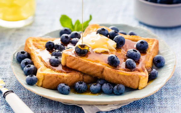 A delicious plate of golden French toast topped with fresh blueberries, syrup, and a pat of butter, set against a soft blue backdrop, creating a vibrant breakfast scene.